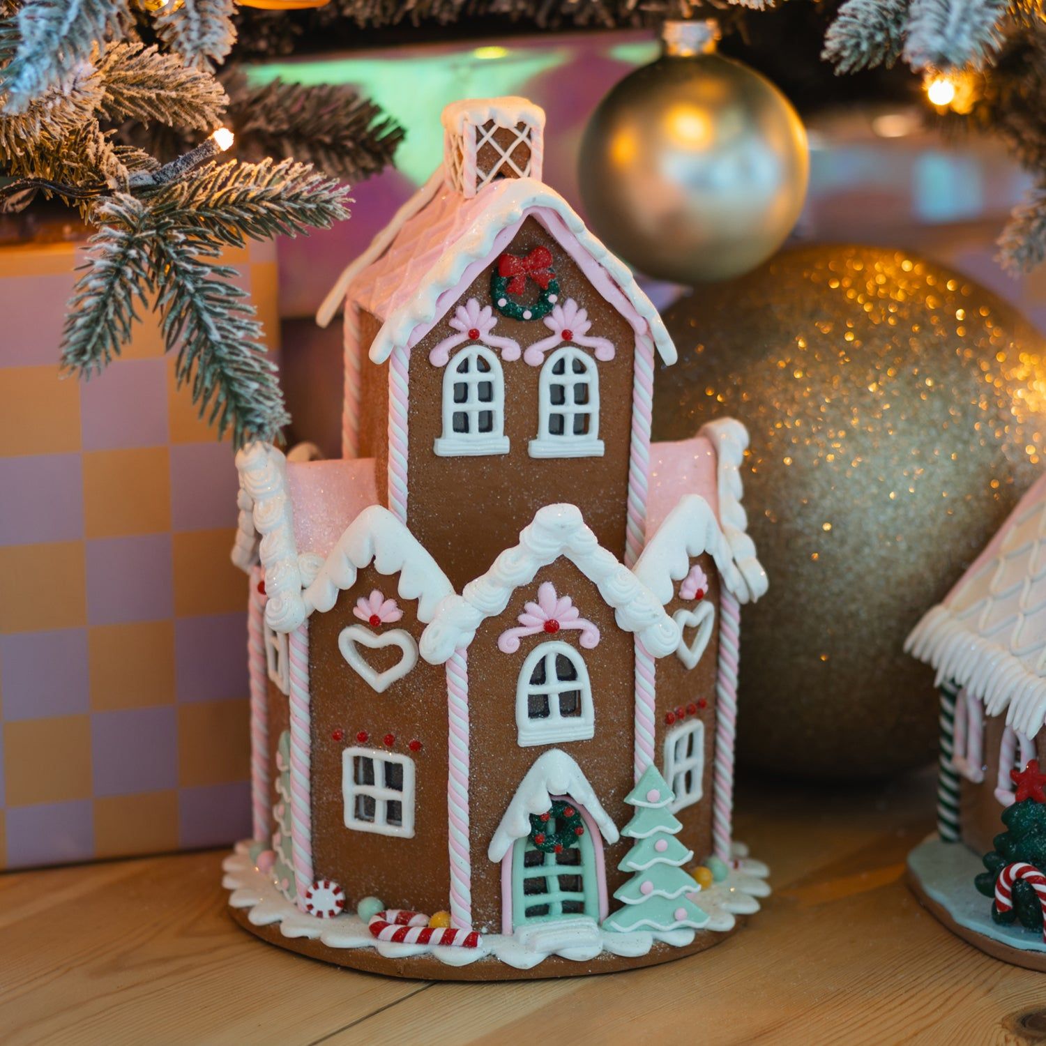 Charming Pink-Iced Gingerbread House Near Christmas Tree Charming Pink-Iced Gingerbread House Near Christmas Tree — Gingerbread Christmas Decor